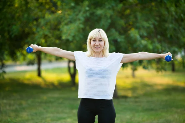 beautiful woman doing sport with dumbbells in summer park