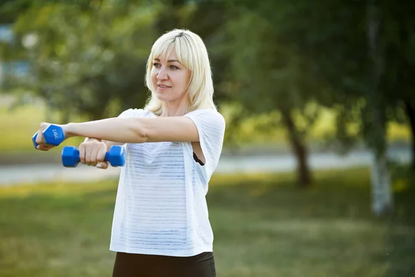 beautiful woman doing sport with dumbbells in summer park