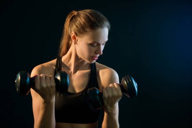 güzel genç kız dumbbells ile spor için bir siyah arka plan üzerine gider