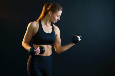 güzel genç kız dumbbells ile spor için bir siyah arka plan üzerine gider