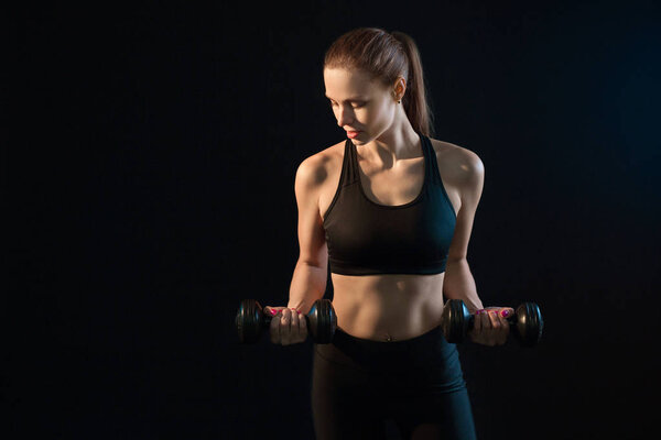 beautiful young girl goes in for sports with dumbbells on a black background