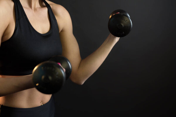body of a young muscular girl with dumbbells on a black background