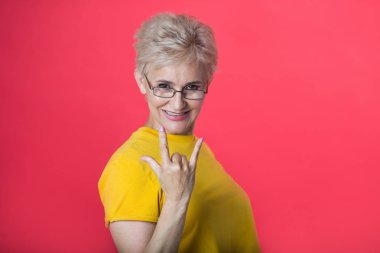 kısa saç kesimi ve bir jest bir kırmızı zemin üzerine sarı bir tişört giyen gözlük el ile şık yaşlı kadın