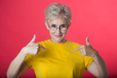 kısa saç kesimi ve bir jest bir kırmızı zemin üzerine sarı bir tişört giyen gözlük el ile şık yaşlı kadın