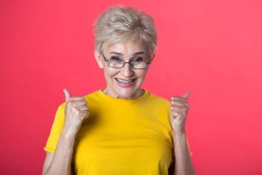 kısa saç kesimi ve bir jest bir kırmızı zemin üzerine sarı bir tişört giyen gözlük el ile şık yaşlı kadın