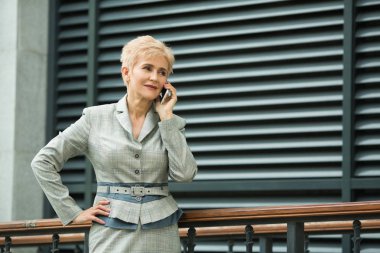 duvarın yanında telefonda konuşurken yaz aylarında bir kısa saç modeli ile bir takım elbise ile yaşta şık modern kadın