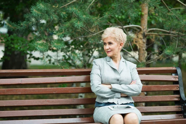 stylish elderly woman with a short haircut sitting on a bench with in a park in summer