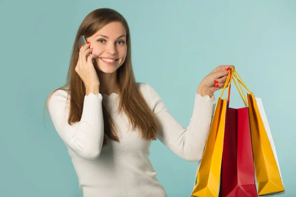 Bela Jovem Segurando Sacos Compras Fundo Azul Falando Telefone — Fotografia de Stock