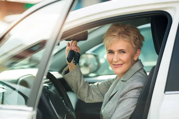 yaş, takım elbiseli şık kadın elinde tuşları ile yaz aylarında bir arabanın direksiyonuna oturur