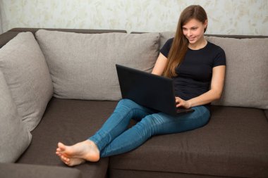 güzel genç kızı evde bir dizüstü bilgisayar ile kanepede oturan siyah t-shirt