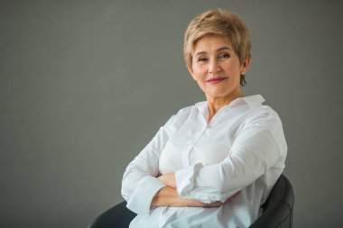 gri bir arka plan üzerinde Beyaz gömlekli bir kısa saç kesimi ile şık bir yaşlı kadın portresi
