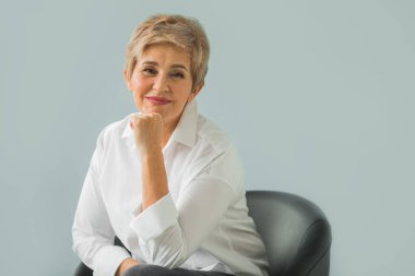 Mavi bir arka plan üzerinde Beyaz gömlekli bir kısa saç kesimi ile şık bir yaşlı kadın portresi