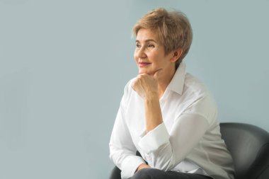 Mavi bir arka plan üzerinde Beyaz gömlekli bir kısa saç kesimi ile şık bir yaşlı kadın portresi