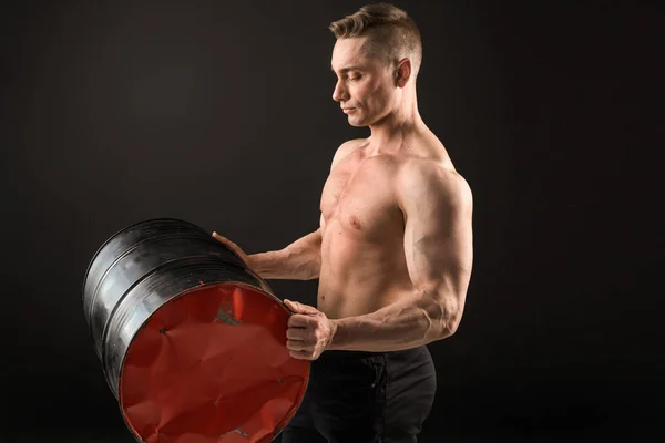 handsome muscular man on a black background holding an iron barrel