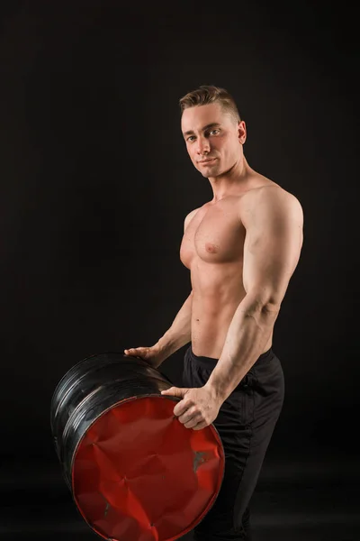 handsome muscular man on a black background holding an iron barrel