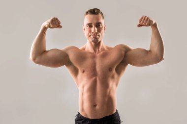 gri arka planda pompalanmış kaslar ile yakışıklı erkek atlet