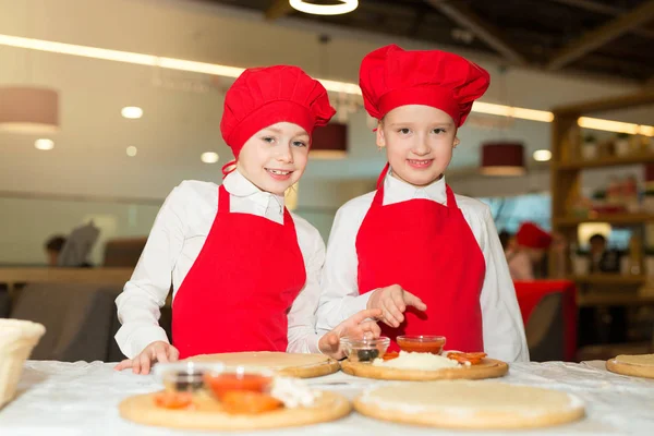 two beautiful cook girls in white shirts and red aprons in the restaurant make pizza