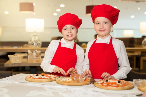 two beautiful cook girls in white shirts and red aprons in the restaurant make pizza