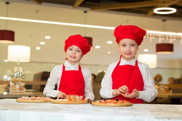 two beautiful cook girls in white shirts and red aprons in the restaurant make pizza