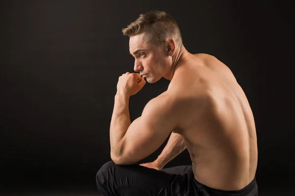 handsome man with muscles on a black background sitting back
