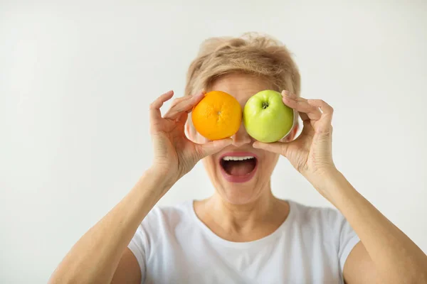 beautiful aged woman with short haircut in a white t-shirt with an apple and an orange on a white background