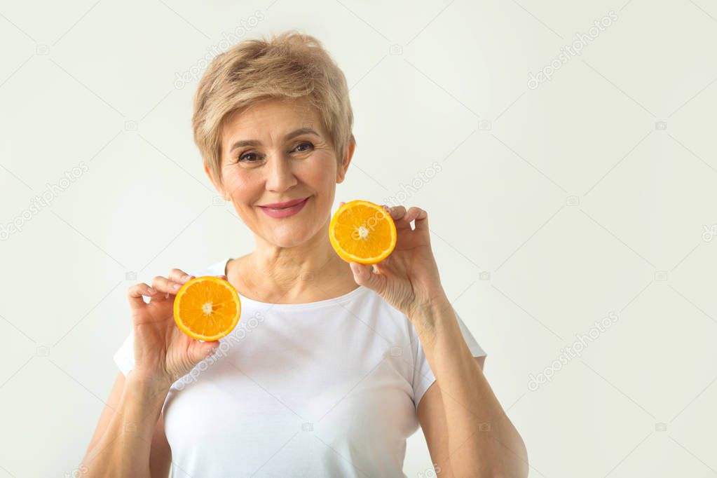 beautiful aged woman with a short haircut in a white T-shirt with oranges in her hands on a white background