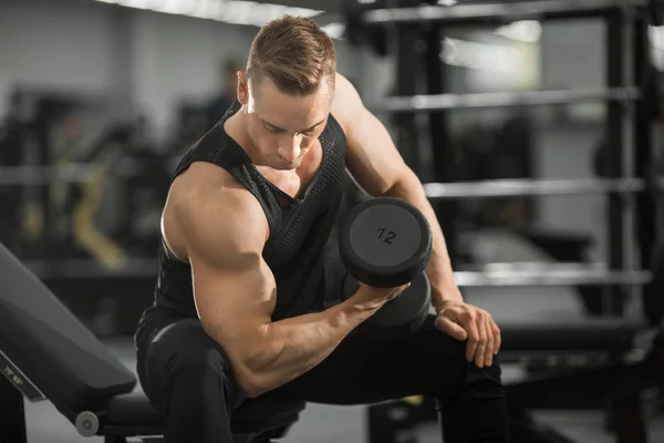 handsome man in good shape with muscles in the gym exercising exercises with dumbbells