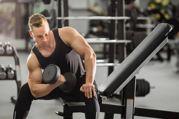 handsome man in good shape with muscles in the gym exercising exercises with dumbbells