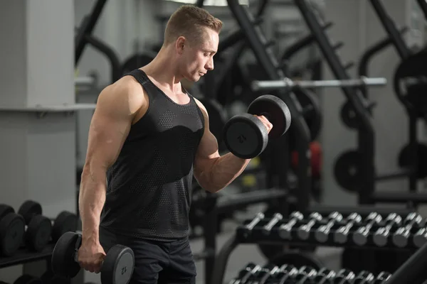 handsome man in good shape with muscles in the gym exercising exercises with dumbbells