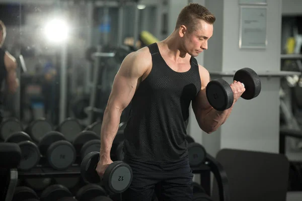 handsome man in good shape with muscles in the gym exercising exercises with dumbbells