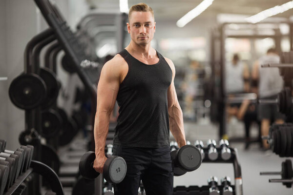 красивый мужчина в хорошей форме с мышцами в тренажерном зале упражнения с гантелями
