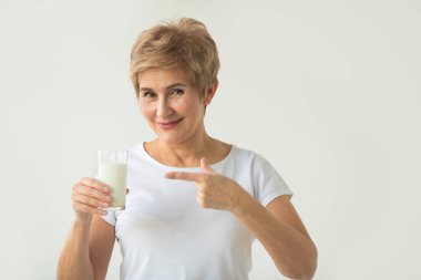 el bir jest ile beyaz bir arka plan üzerinde süt bir bardak ile beyaz bir t-shirt güzel yaşlı kadın