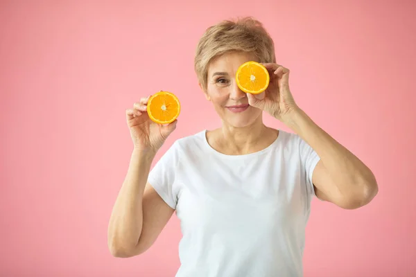 pembe bir arka plan üzerinde elinde bir portakal ile beyaz bir t-shirt güzel yaşlı kadın