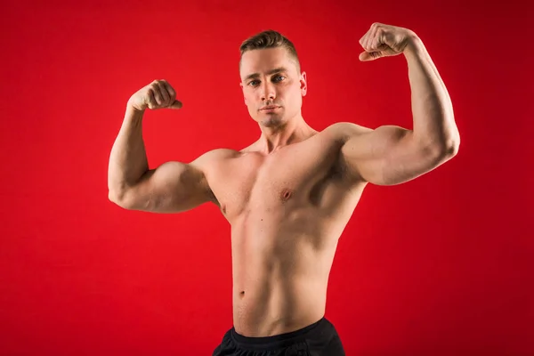 Joven Guapo Forma Atlética Sobre Fondo Rojo Muestra Sus Músculos —  Fotos de Stock