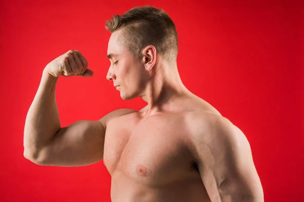 Joven Guapo Forma Atlética Sobre Fondo Rojo Muestra Sus Músculos —  Fotos de Stock