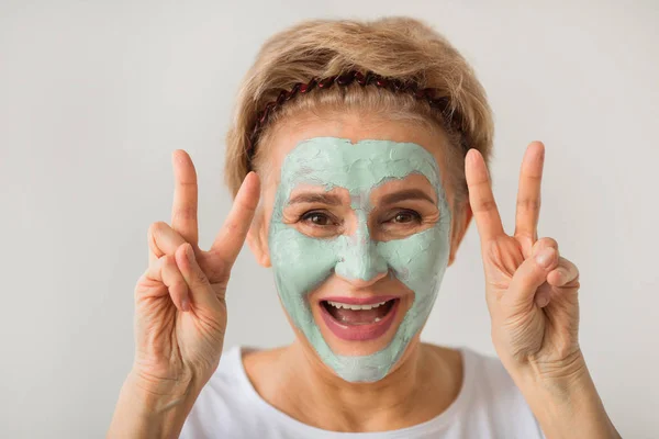 beyaz bir arka plan üzerinde bir sağlıklı yaşam kremi yüz maskesi ile neşeli olumlu güzel yaşlı kadın