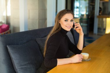 makyaj ve saç modeli ile güzel genç kız bir fincan kahve ile bir restoranda telefonda konuşurken
