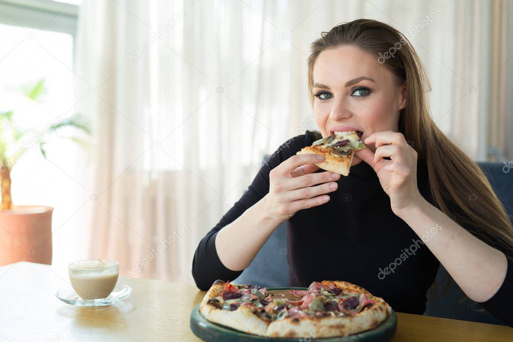 beautiful young woman at the table eats pizza in a restaurant