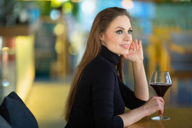bir restoranda bir kadeh şarap ile masada oturan güzel genç kadın