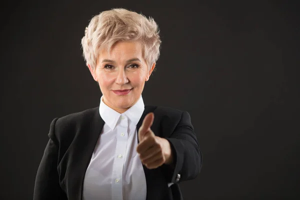 stylish elderly woman with a short haircut in a black suit on a black background with a hand gesture