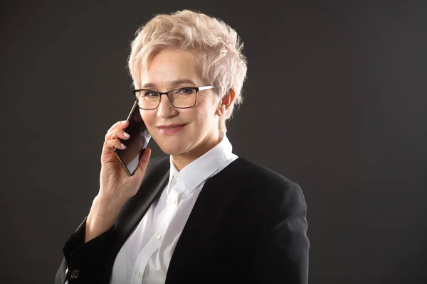 stylish elderly woman in glasses and in a black jacket is calling by phone