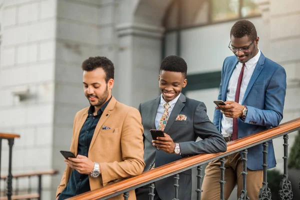 three young friendly men in suits with phones in their hands