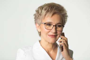 beyaz arka planda beyaz bir ceket gözlük giyen kısa bir saç kesimi ile yetişkin bir kadının portresi telefon görüşmeleri yapar