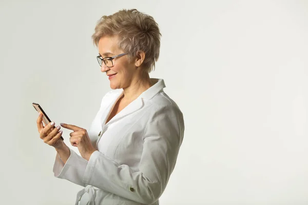 portrait of an adult woman with a short haircut wearing glasses in a white jacket on a white background with a phone in her hand