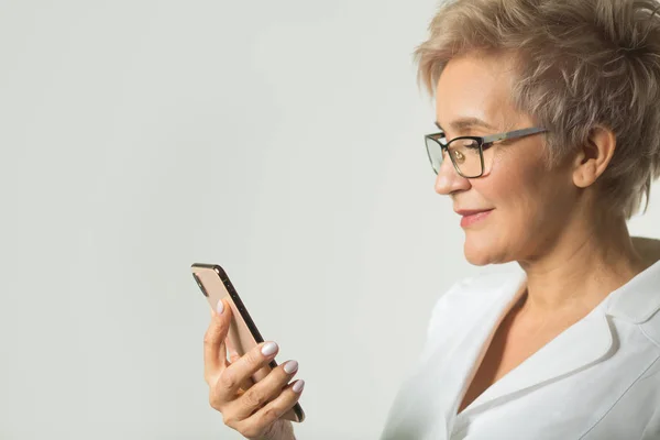 portrait of an adult woman with a short haircut wearing glasses in a white jacket on a white background with a phone in her hand
