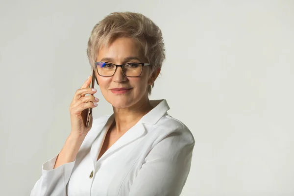 portrait of an adult woman with a short haircut wearing glasses in a white jacket on a white background makes phone calls