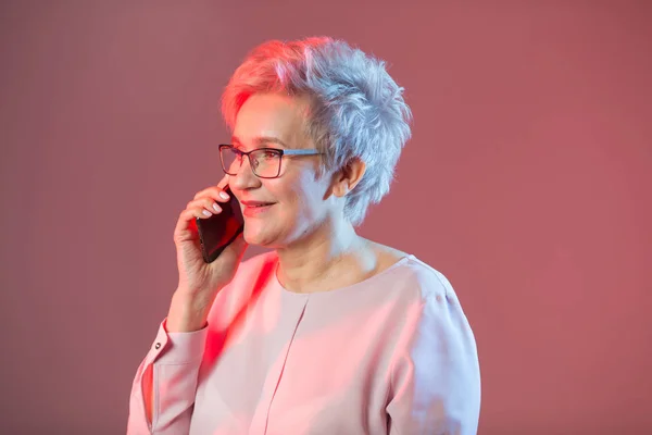 Stijlvolle Oudere Vrouw Glazen Met Een Telefoon Een Roze Achtergrond — Stockfoto