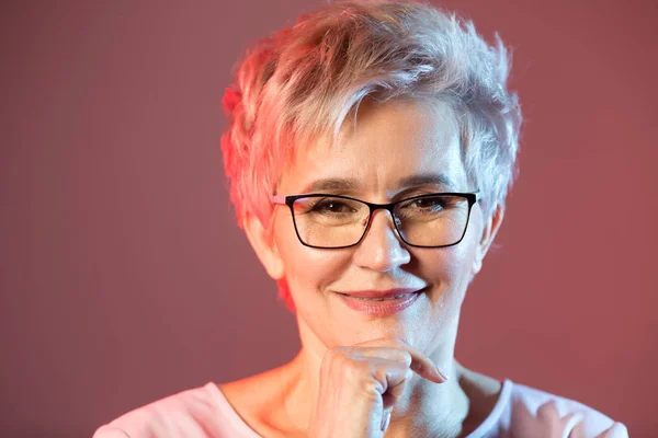 portrait of an old woman with glasses on a pink background