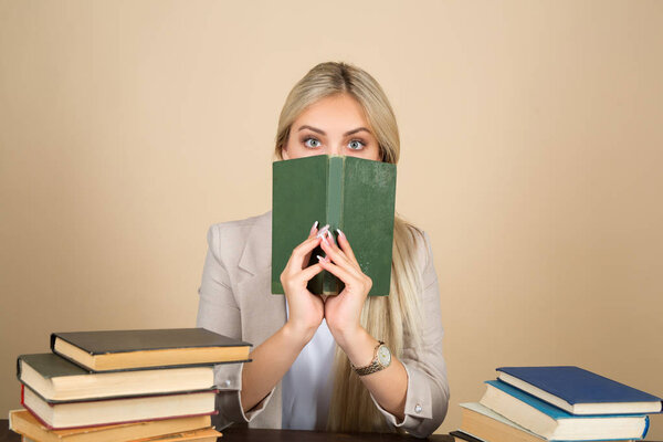 красивая молодая женщина в костюме сидит за столом с книгами с удивленным лицом
