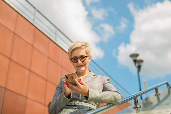 stylish woman in a suit and short-cut glasses with a phone in her hands